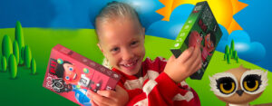 Smiling child holding two colorful kids' game boxes against a bright cartoon landscape with an owl illustration on the right sleeve.