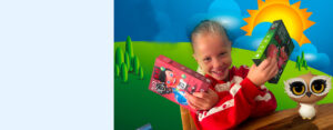 Smiling girl in red holds two colorful kids' game boxes in a bright cartoon landscape with a sun and owl on a table.