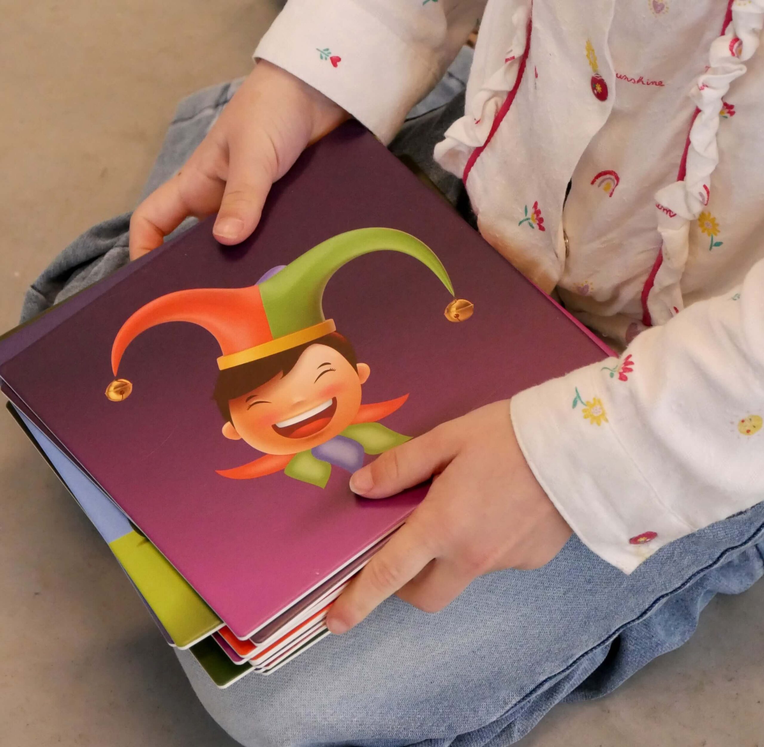 Child in light pajamas sits cross-legged, holding a purple book with a cartoon boy on the cover.