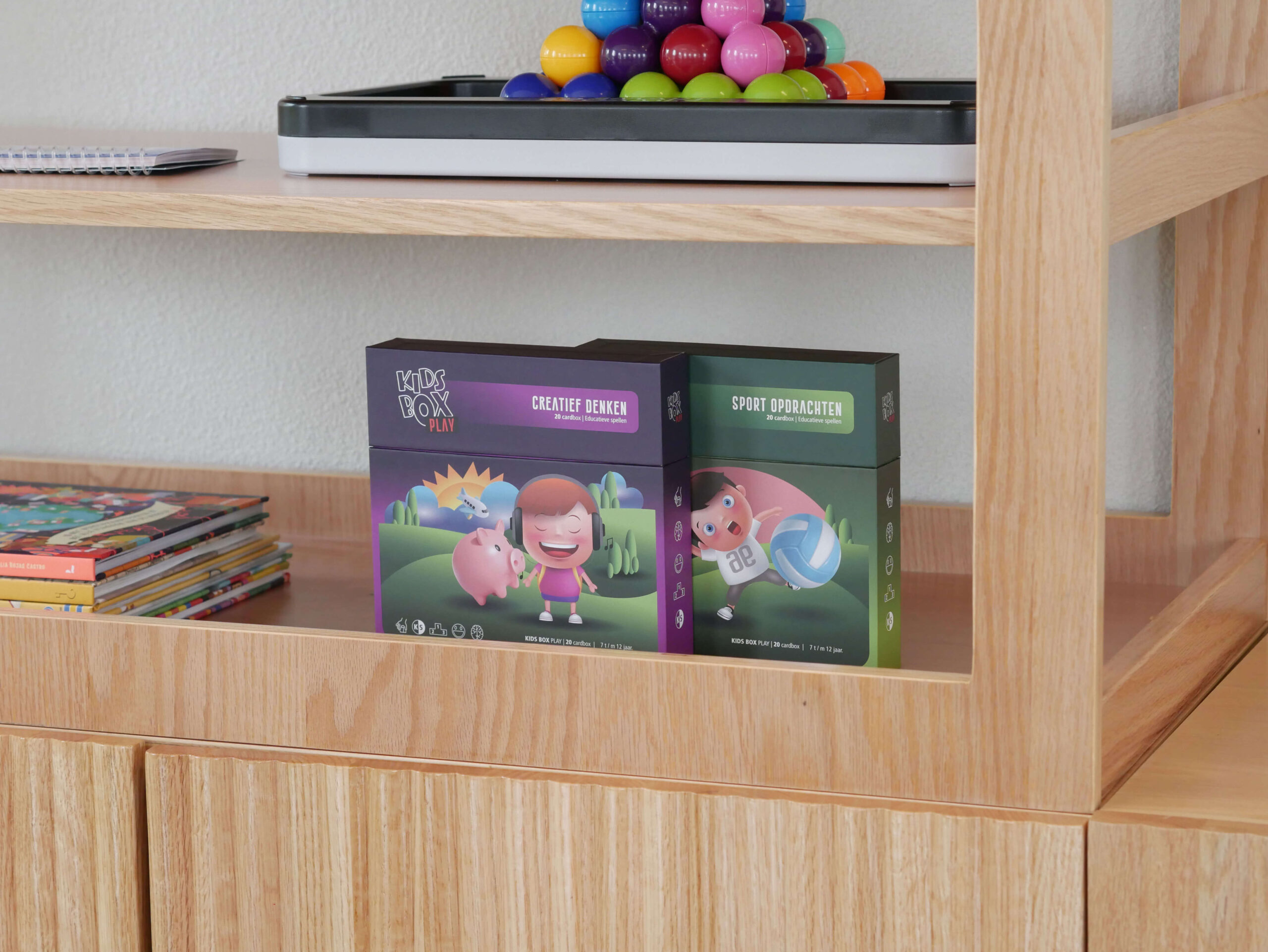 Wooden shelf with a tray of multicolored marbles on the top shelf and boxed kids' games on the lower shelf.