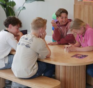 Four children seated around a curved wooden table, shaping a small clay object together at a group activity center.