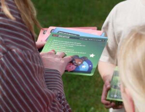 Two people hold colorful game cards outdoors on a grassy surface